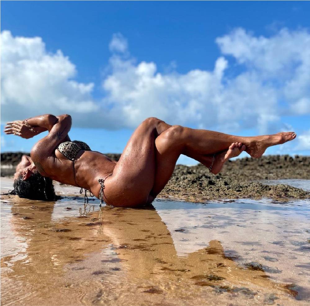 Beth Pedote fazendo posição de yoga em praia.